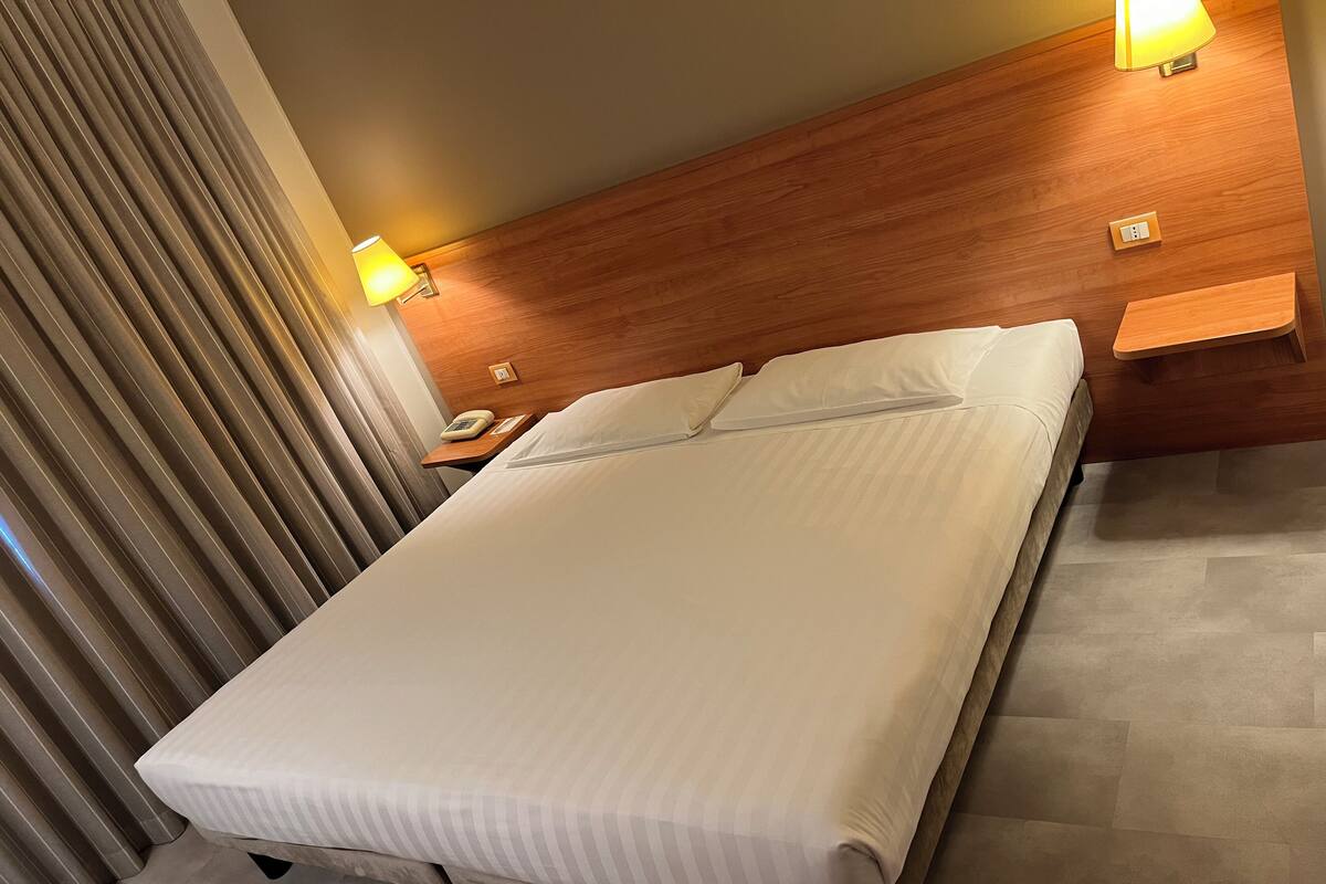 Une chambre d’hôtel avec un lit, une tête de lit en bois, des lampes de chevet, une table de chevet et un téléphone.