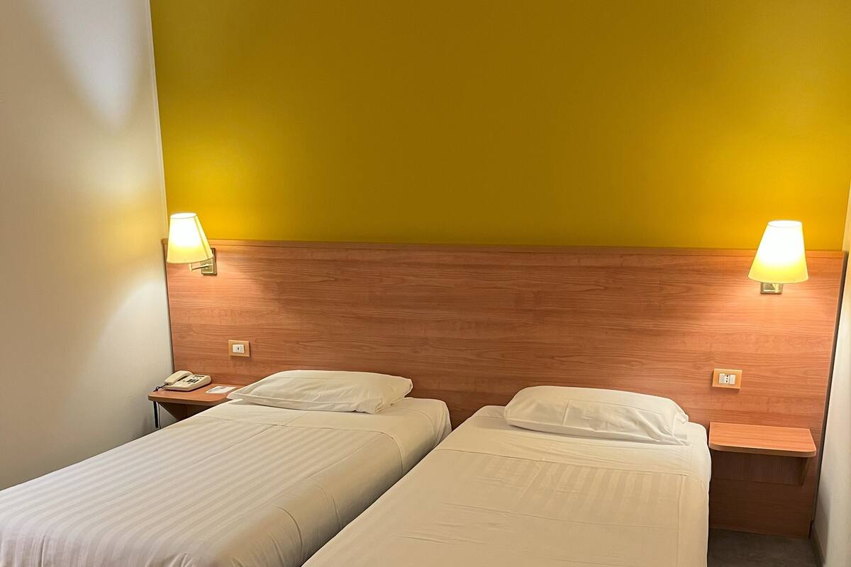 Une chambre d’hôtel avec deux lits simples, une tête de lit en bois, des lampes de chevet et un téléphone sur la table de chevet.