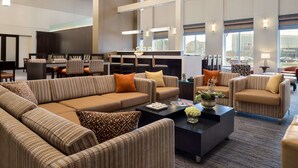 A spacious hotel lobby with a large seating area, a bar, and a view of the city. - Hampton Inn & Suites Rosemont Chicago O'Hare (Rosemont)