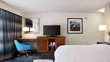 A hotel room with a bed, a desk with a television, a chair, a desk lamp, and a framed picture on the wall.