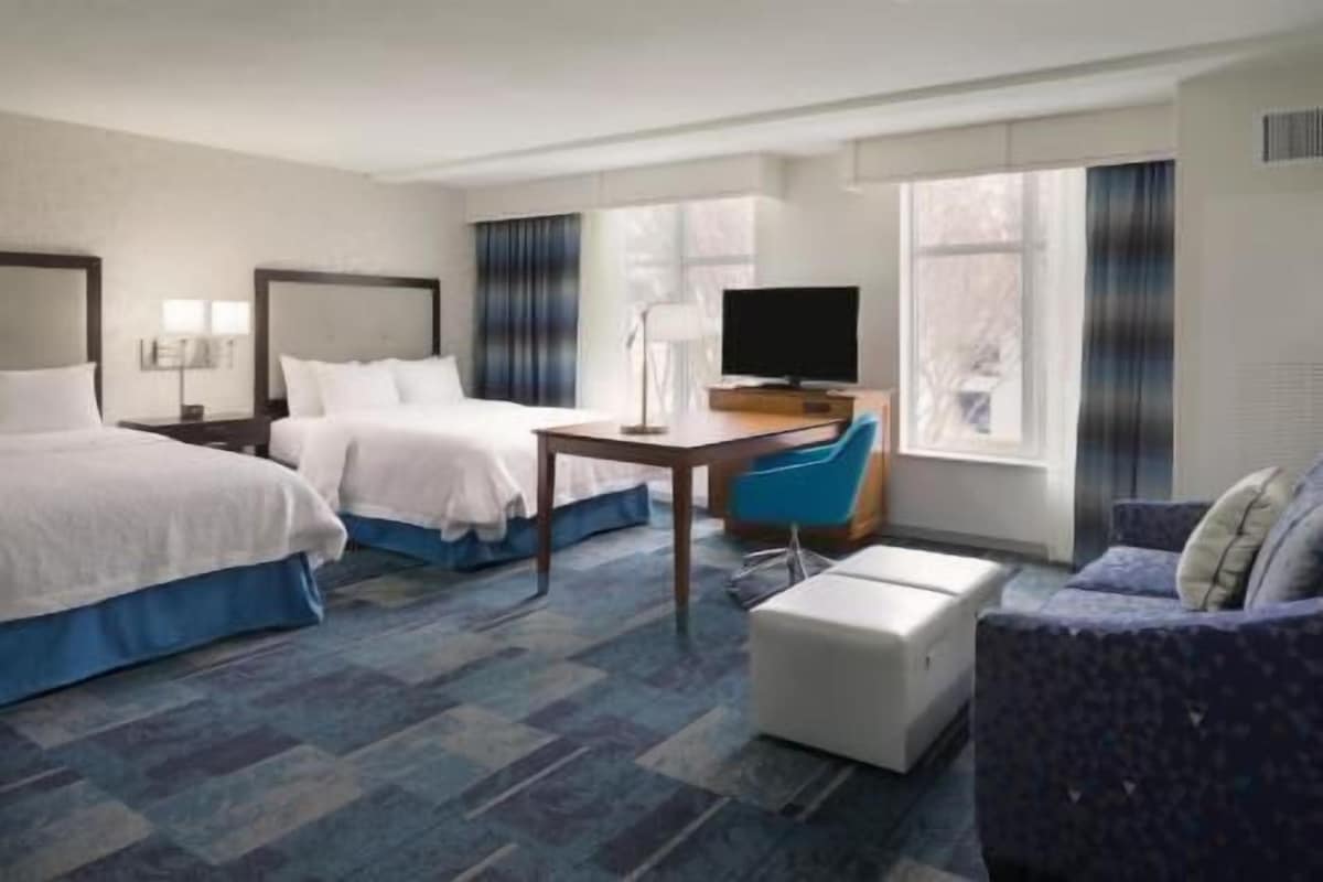 A hotel room with two beds, a desk, a television, and a couch.