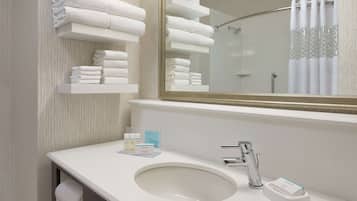 Un baño con un lavamanos blanco, un espejo y repisas con toallas dobladas ordenadamente.