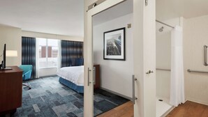 A hotel room with a bed, a desk, a chair, a shower, and a window with curtains. - Hampton Inn & Suites Rosemont Chicago O'Hare (Rosemont)