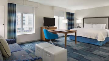 Habitación de hotel con cama, escritorio con televisor, silla, sofá y ventana con cortinas.