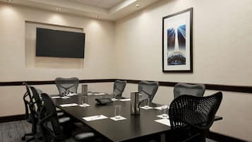 A conference room with a long table, six chairs, a projector screen, and a framed picture on the wall.