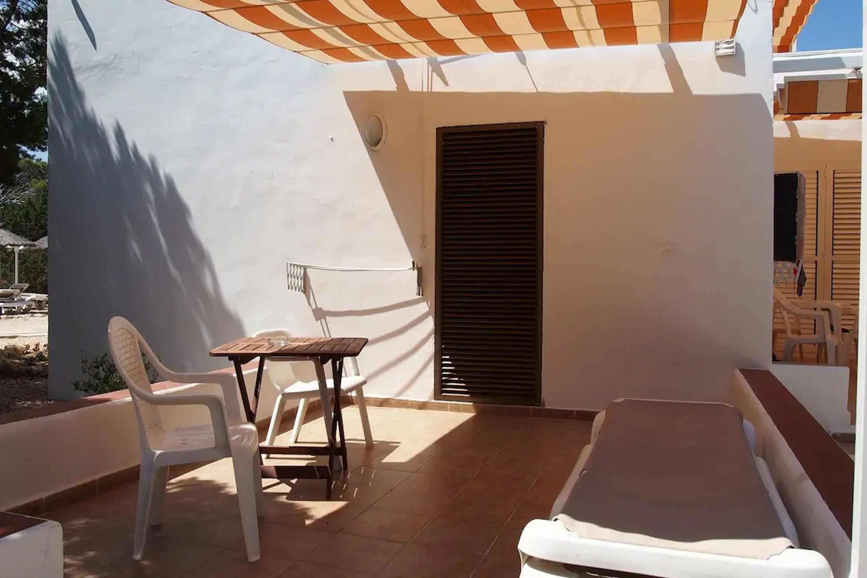 A small balcony with a table and chairs, a covered area, and a bed.