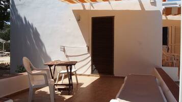 A small balcony with a table and chairs, a covered area, and a bed.