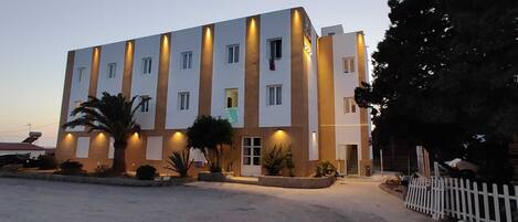 A multi-story hotel with a modern design, featuring a central courtyard with palm trees and a white picket fence.