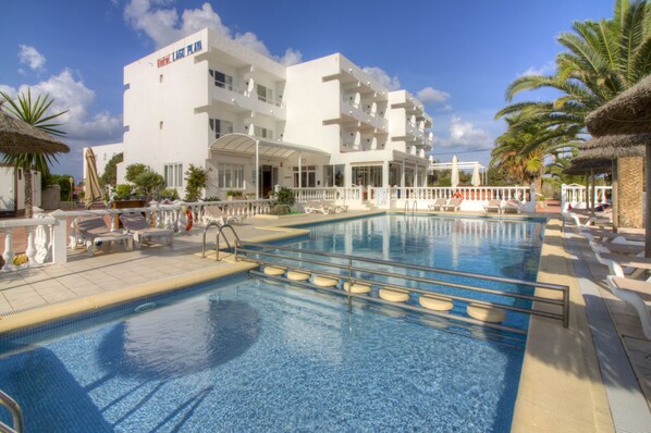 A hotel with a swimming pool, lounge chairs, and palm trees. - Complejo Lago Playa (Formentera)