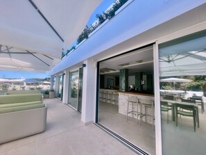 A modern outdoor dining area with a bar, green cushioned seating, and a view of the surrounding landscape. - Complejo Lago Playa (Formentera)