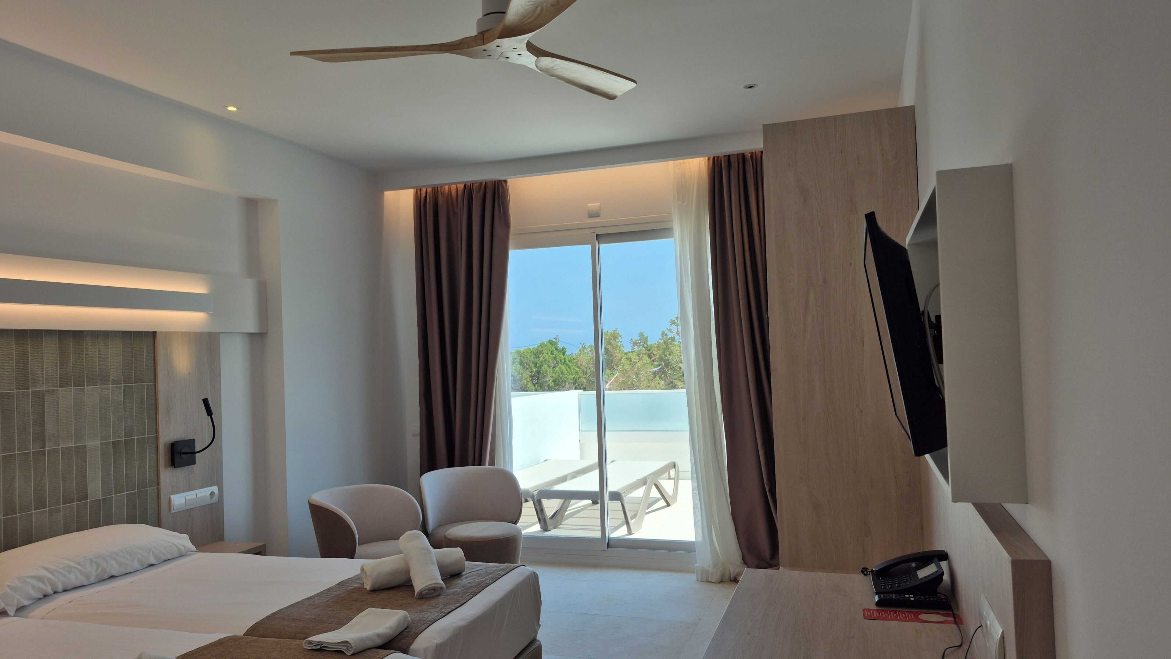 Quarto de hotel com cama, poltrona, televisão e varanda com vista.