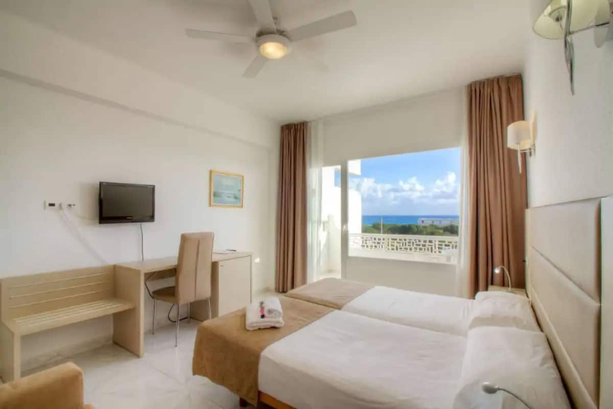 Habitación de hotel con cama, escritorio, silla, televisión y ventana con vista al mar.