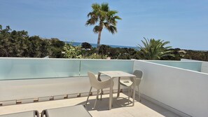 A rooftop terrace with a table and chairs, overlooking a coastal landscape with palm trees and the sea. - Complejo Lago Playa (Formentera)