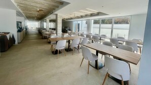 A spacious dining area with long tables and chairs, large windows, and a modern ceiling design. - Complejo Lago Playa (Formentera)