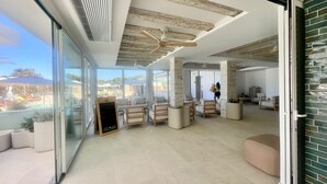 A spacious indoor area with a pool view, wooden ceiling beams, and modern furniture. - Complejo Lago Playa (Formentera)