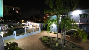 Une cour avec une piscine, des palmiers et un bâtiment dont les fenêtres sont illuminées.