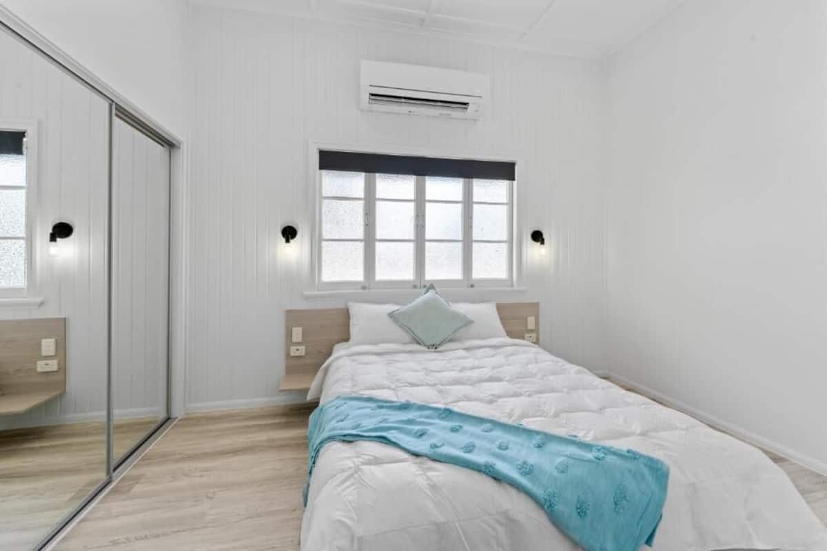 A bedroom with a bed, a window, an air conditioning unit, and a sliding door.