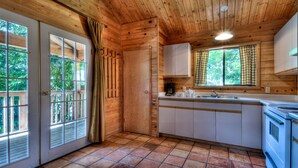 A wooden cabin kitchen with a tiled floor, a stove, cabinets, a sink, and a window with curtains. - Heriot Bay Inn (Quadra Island)