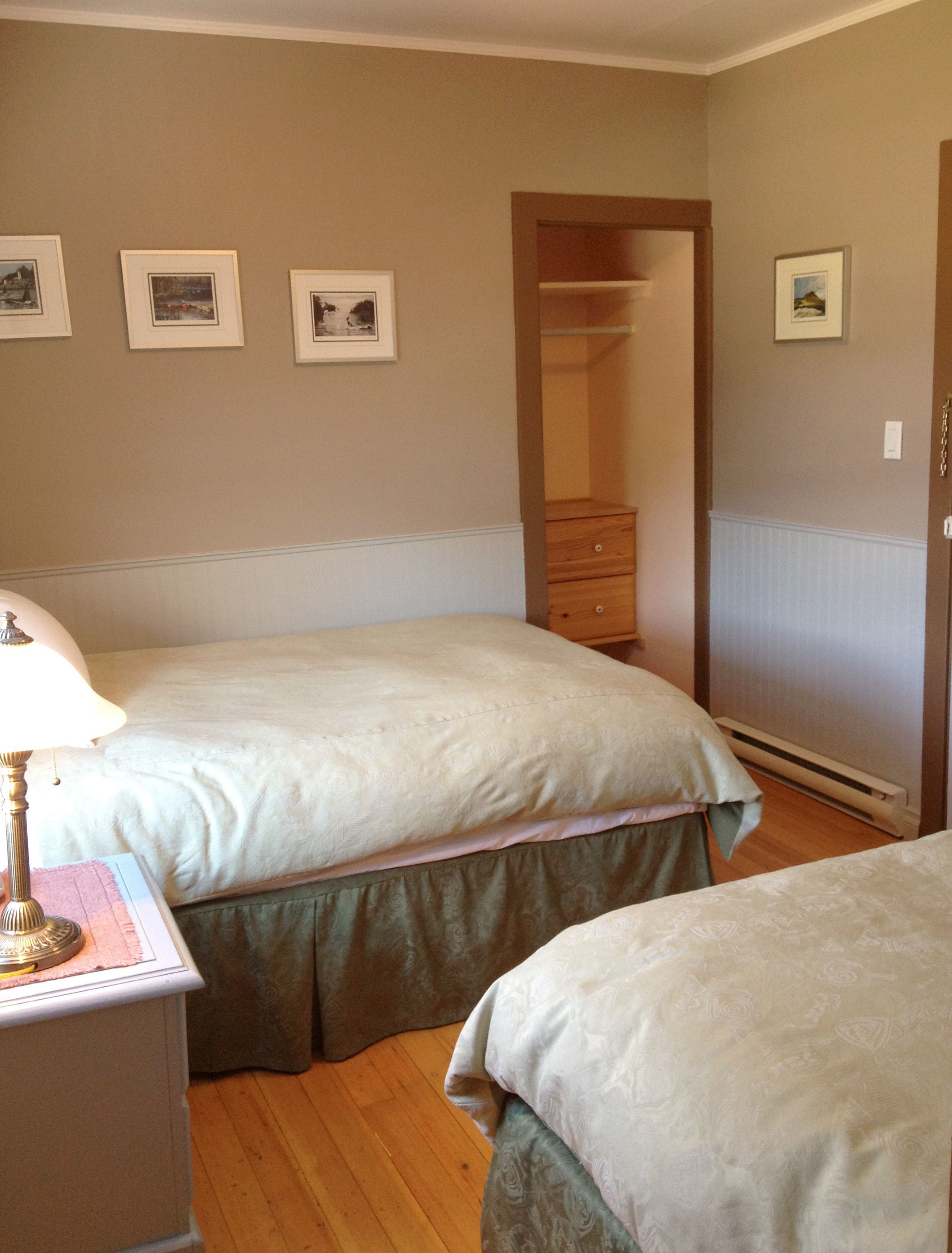 A bedroom with two beds, a dresser, and framed pictures on the wall.
