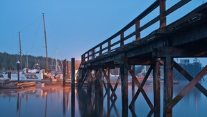 A pier with boats docked, a forested hill in the background, and a clear sky. - Heriot Bay Inn (Quadra Island)