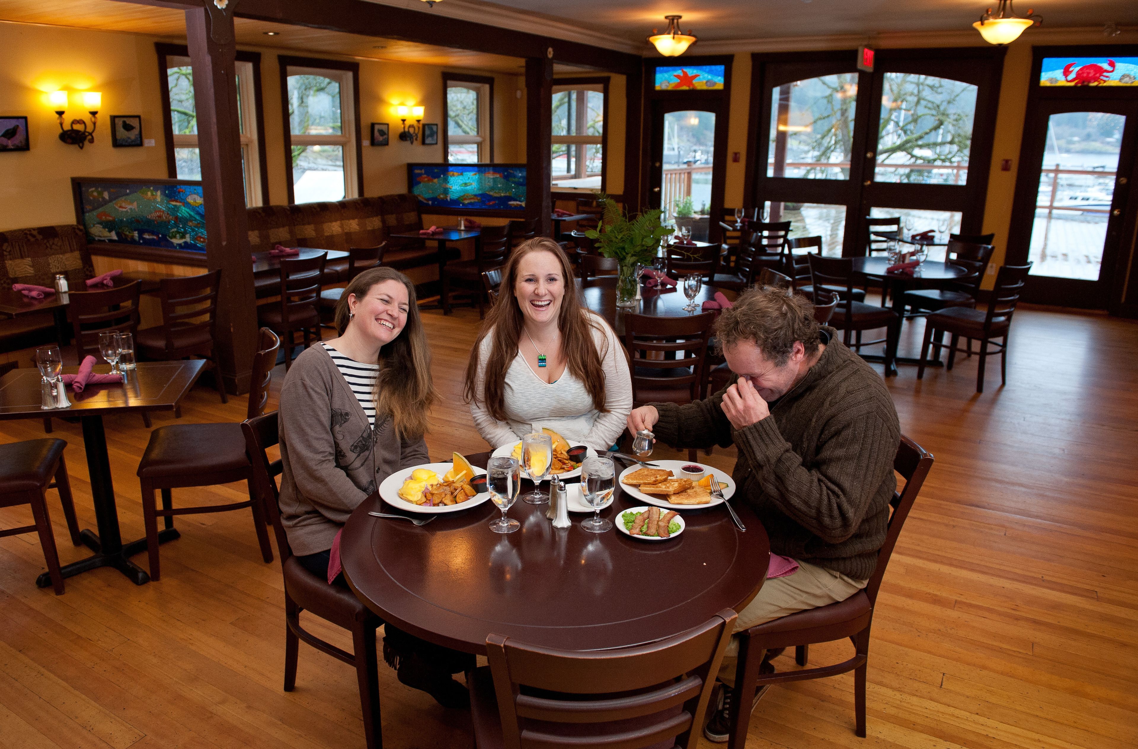 A restaurant with wooden floors and tables, large windows, and artwork on the walls.