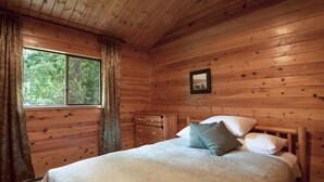 A wooden cabin bedroom with a bed, dresser, and window. - Heriot Bay Inn (Quadra Island)