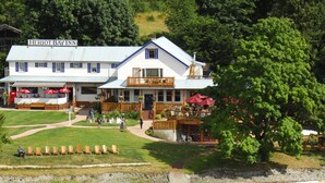 A two-story building with a sign reading "Heriot Bay Inn." There are outdoor seating areas with umbrellas, a pathway leading to the entrance, and a body of water in the foreground. - Heriot Bay Inn (Quadra Island)