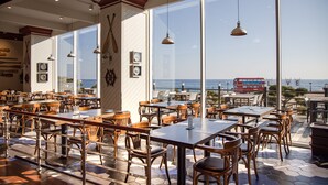 Een restaurant met grote ramen, met uitzicht op de zee en een rode bus in de verte.