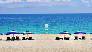 Een strand met rijen blauwe parasols en ligbedden.