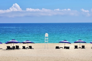 Een strand met rijen blauwe parasols en ligbedden.