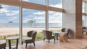 Een modern interieur met grote ramen, houten vloeren en een zithoek met fauteuils en kleine tafels.