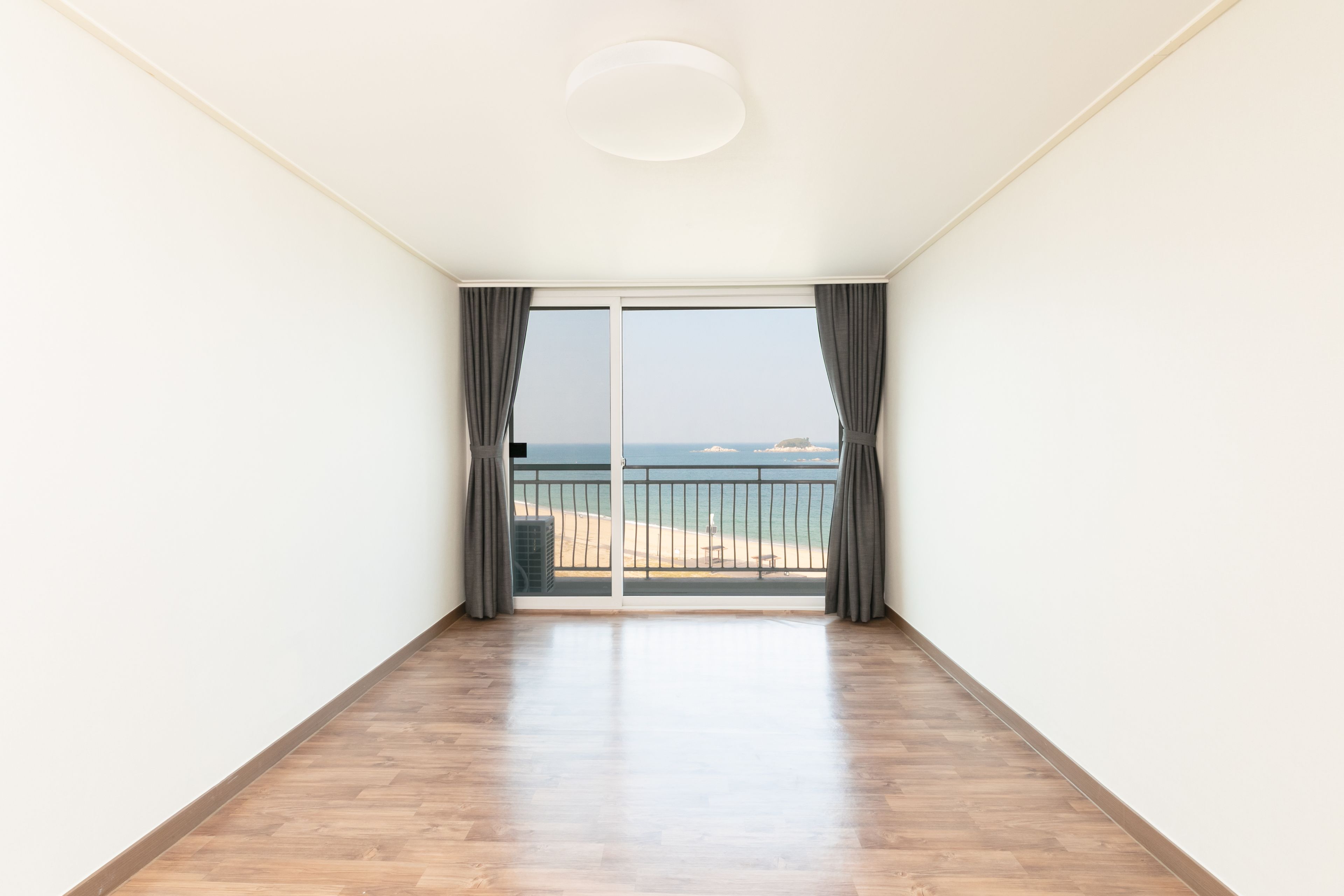 Une pièce dotée d’un plancher en bois, de murs blancs et d’une grande porte-fenêtre coulissante donnant sur un balcon avec vue sur la mer.