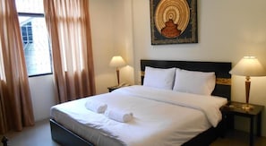 Una cama bien tendida con sábanas blancas y dos almohadas, un cabecero oscuro, dos lámparas de noche y una obra de arte colgada en la pared sobre la cama.