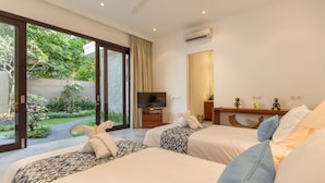A hotel room with two beds, a TV, a desk, and a view of a garden.