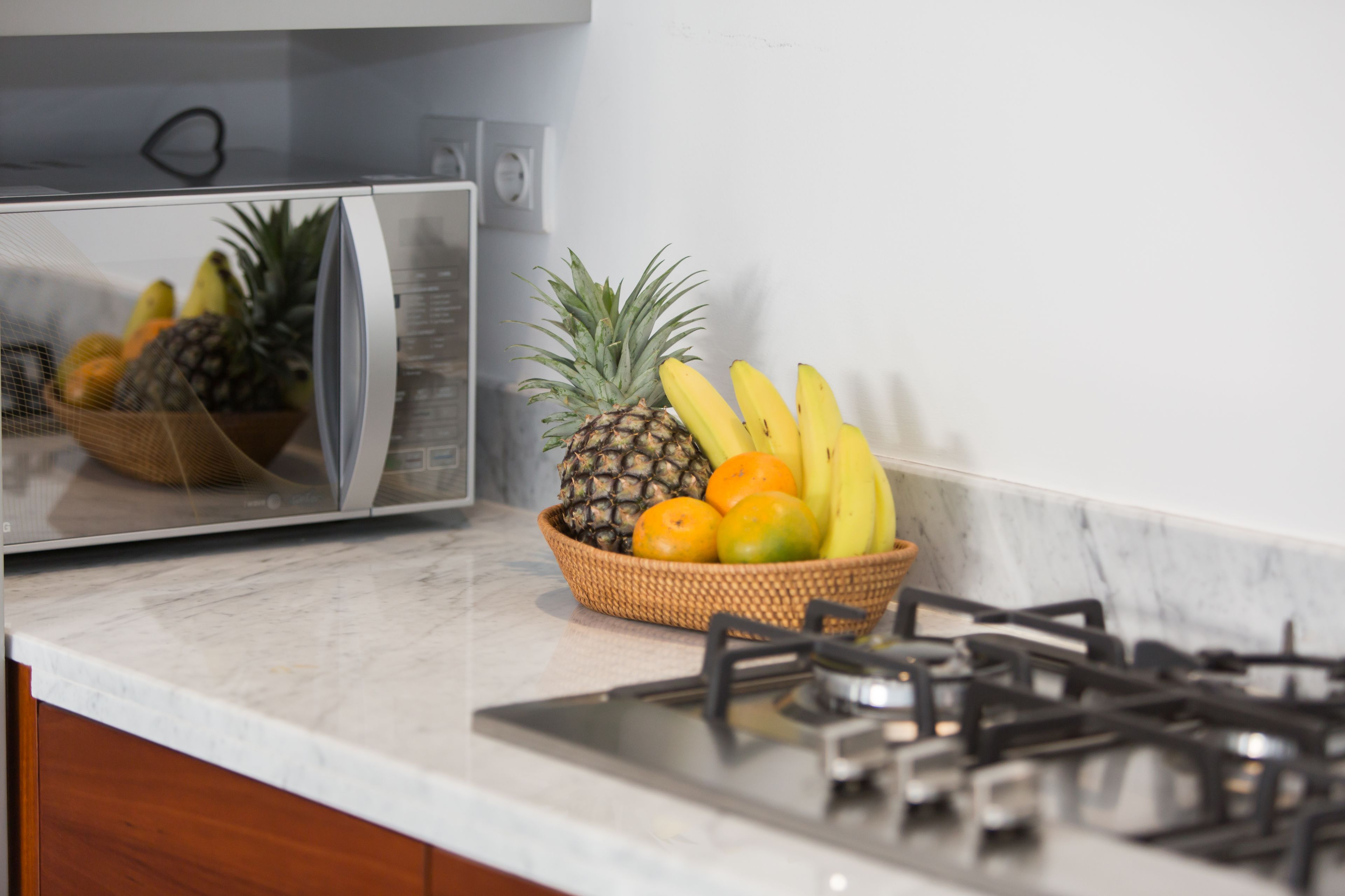 A kitchen with a microwave, a gas stove, and a fruit bowl containing bananas, pineapple, and oranges.