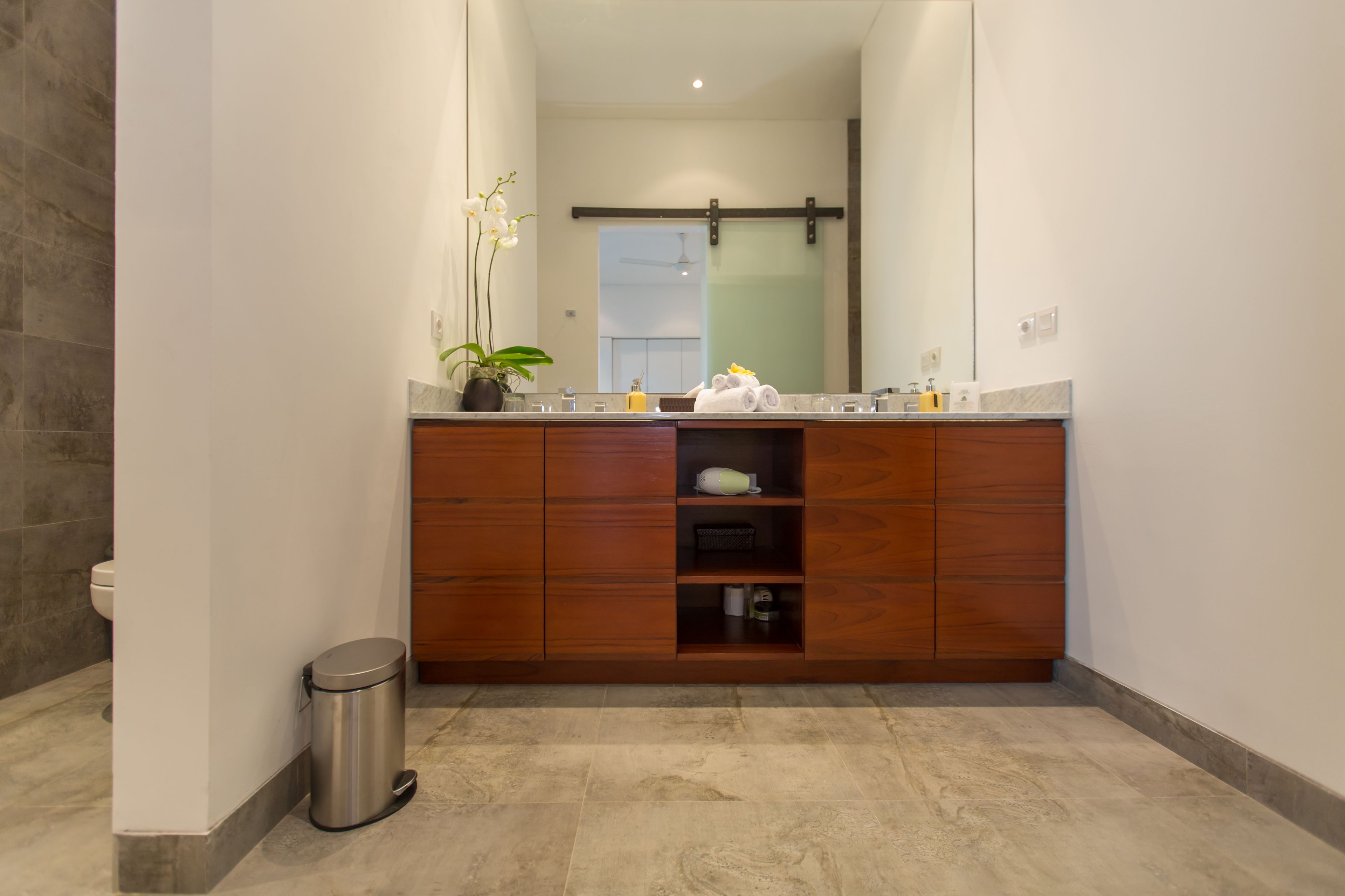 Un baño moderno con tocador de madera, un espejo grande y una orquídea en maceta.