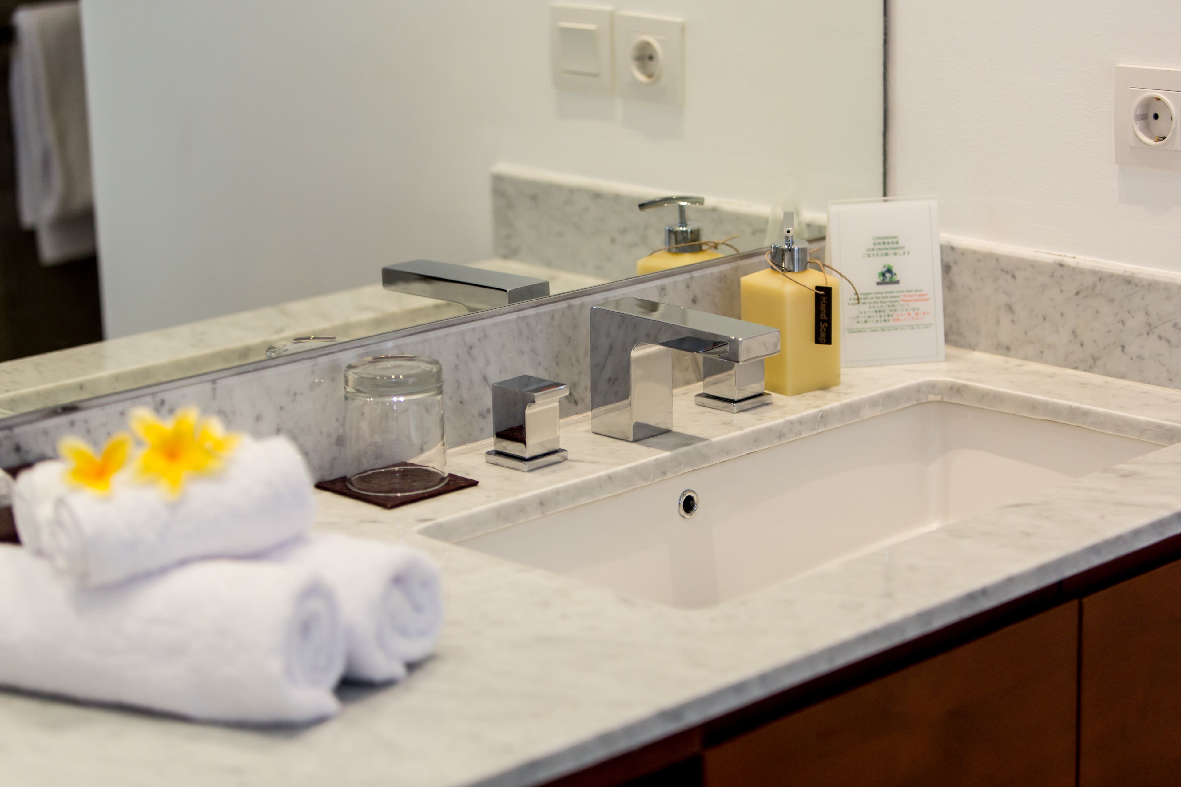 Une salle de bain avec un lavabo en marbre, un miroir, un porte-serviettes avec des serviettes, un distributeur de savon et un verre.