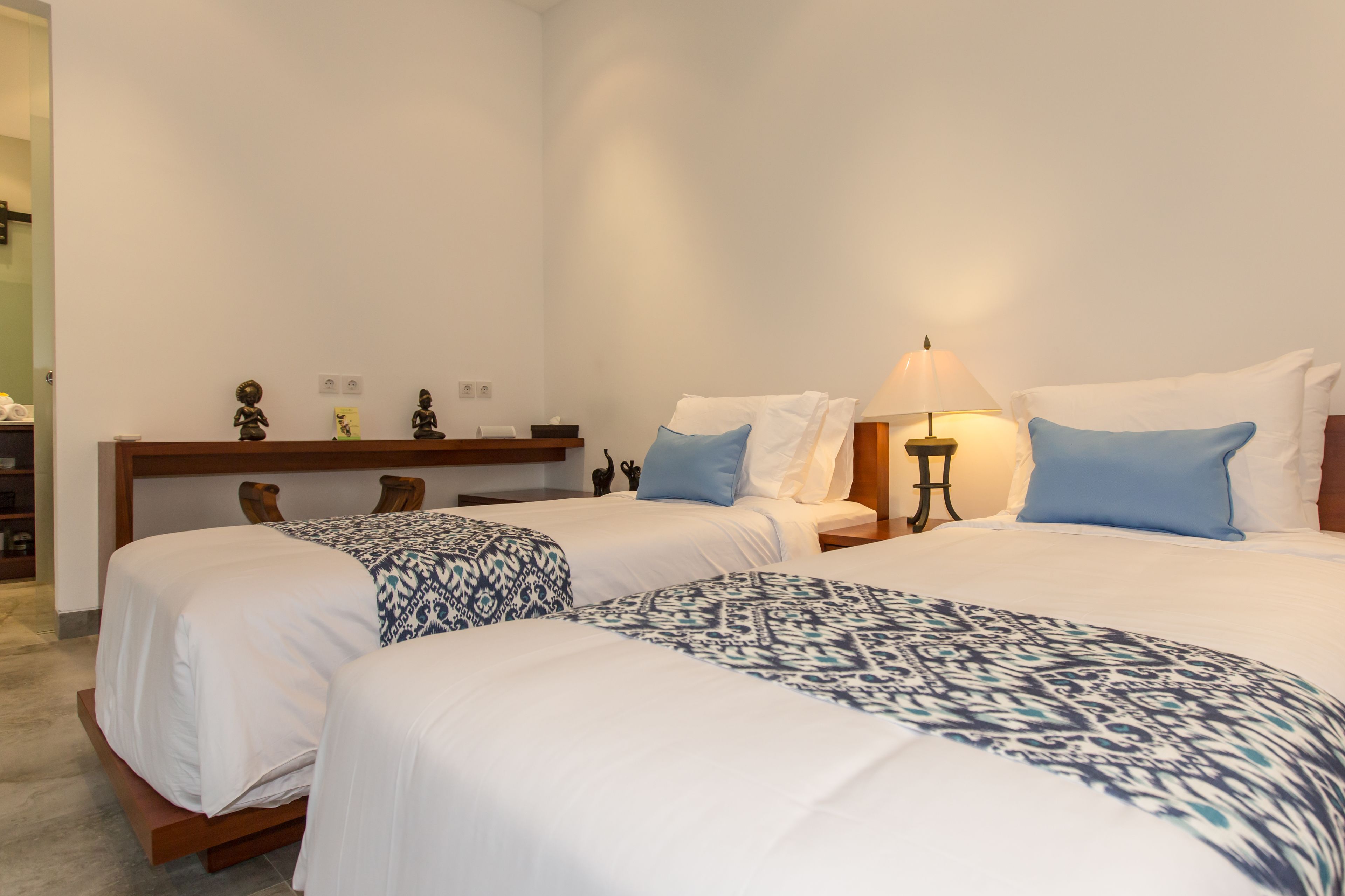 Una habitación de hotel con dos camas, una mesita de noche con lámpara y un estante pequeño con adornos.
