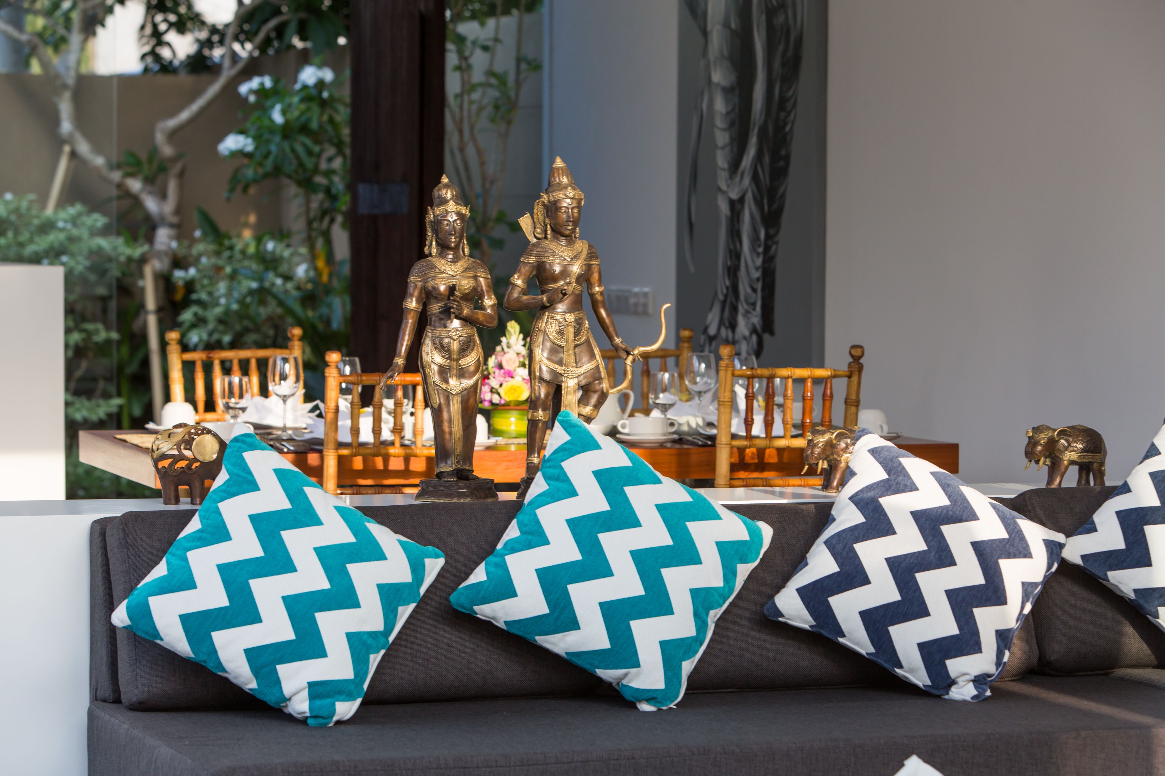 A sofa with patterned cushions, a table with decorative items, and two golden statues.