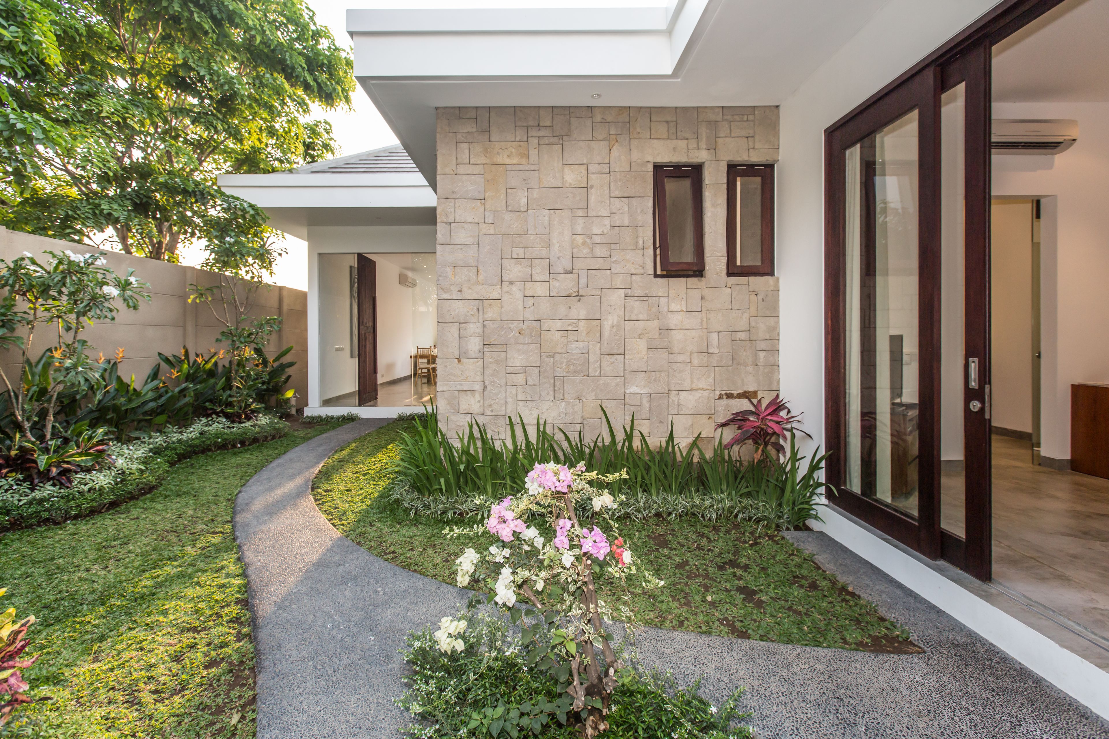 A modern house with a stone exterior, a glass door, and a well-maintained garden with various plants and flowers.