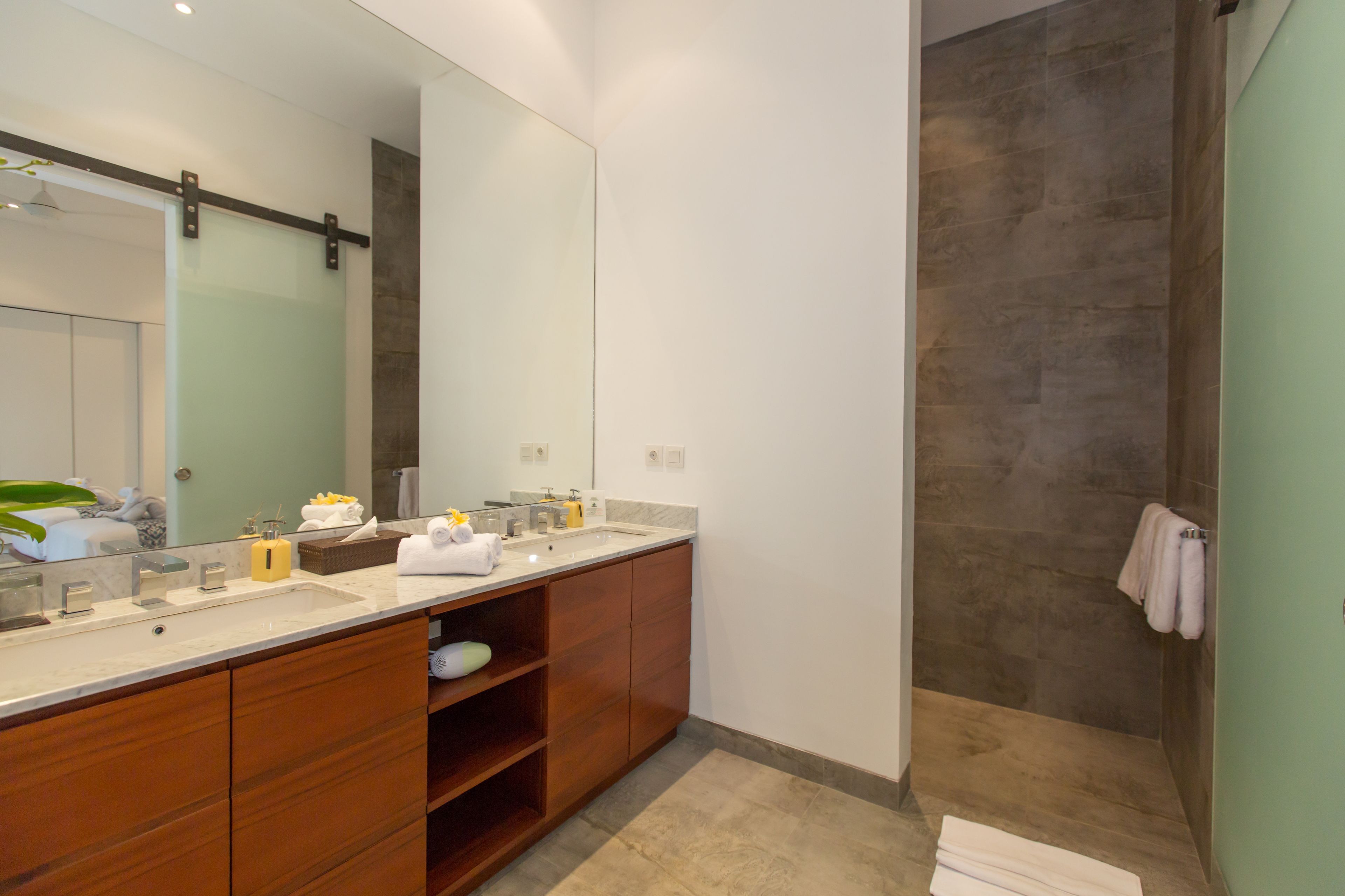 A modern bathroom with a large mirror, wooden vanity, and a shower area.