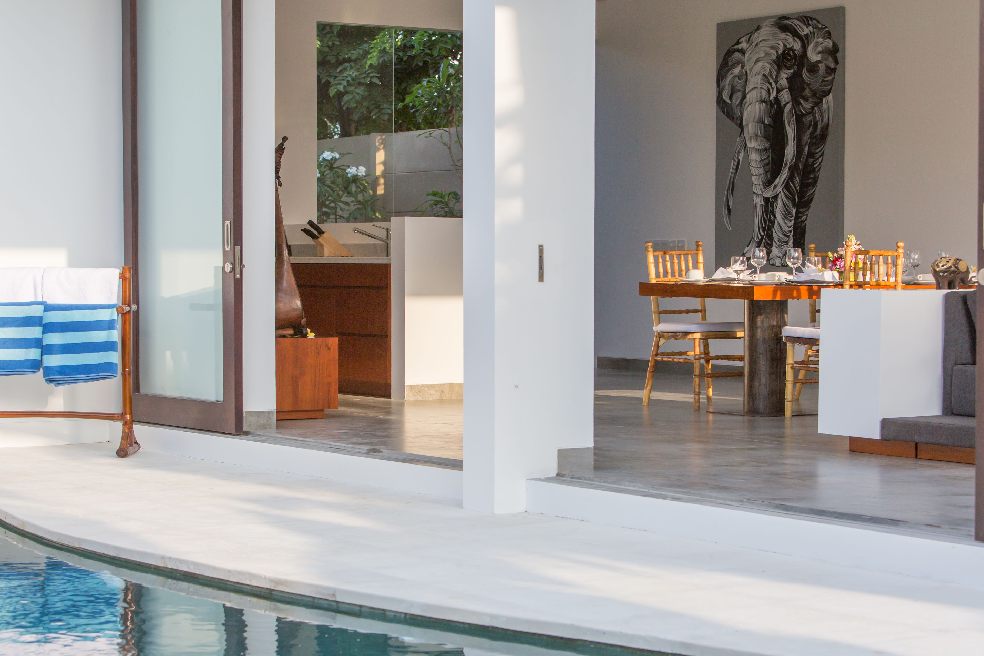 Ein moderner Essbereich mit Blick auf einen Pool, ein großes Elefantenbild und ein Holztisch für zwei Personen.