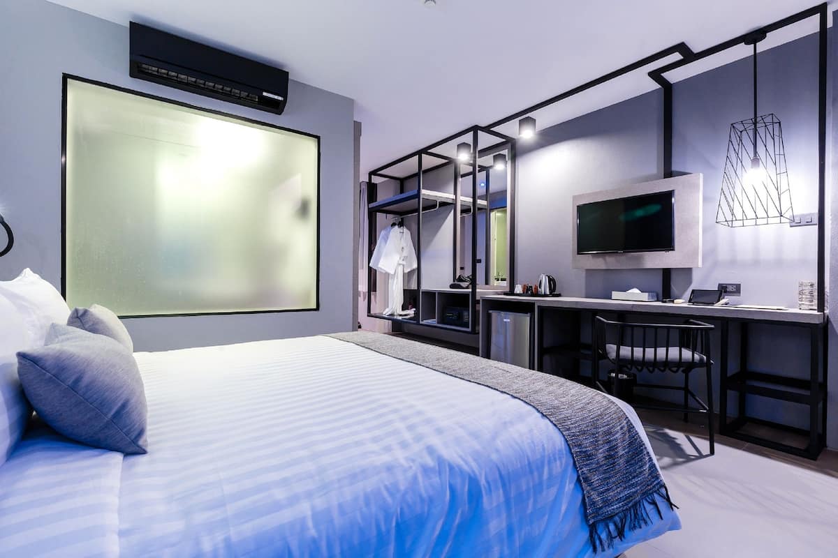 A modern hotel room with a large bed, a desk with a computer, a TV, and a wardrobe.