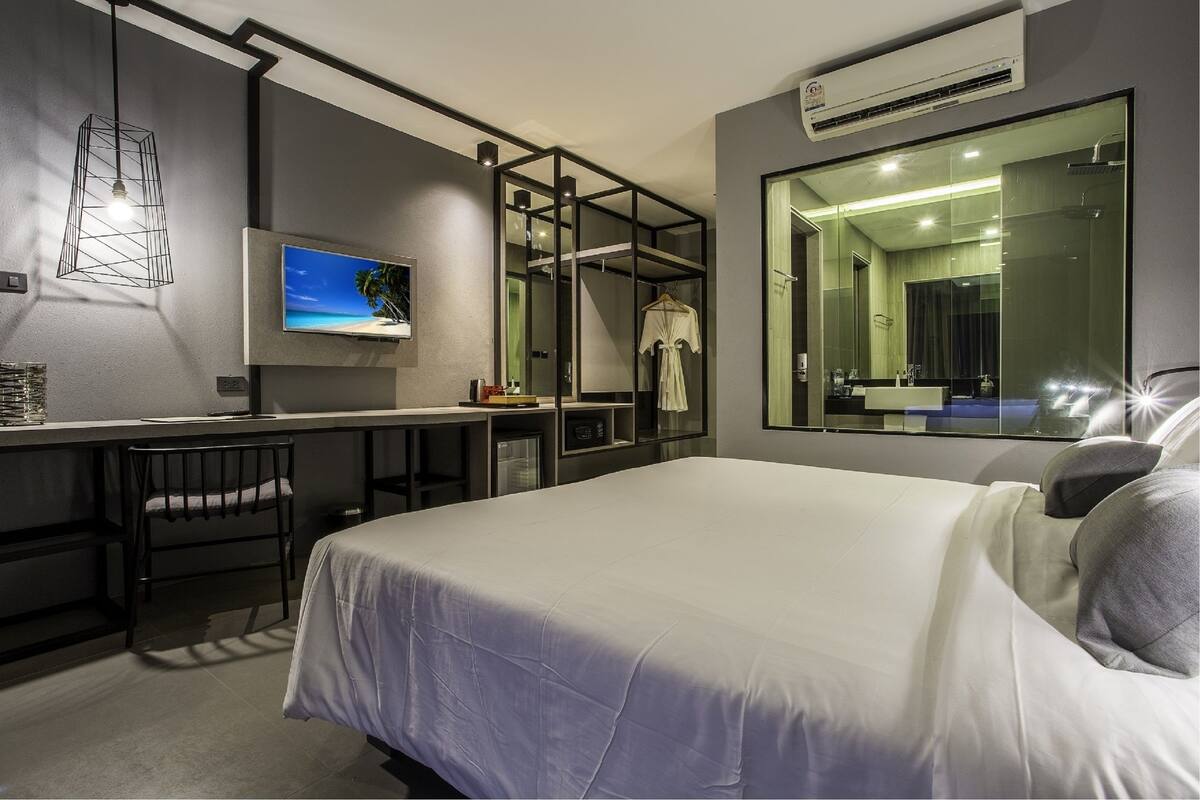 A modern hotel room with a large bed, a desk with a chair, a TV, and a large mirror.