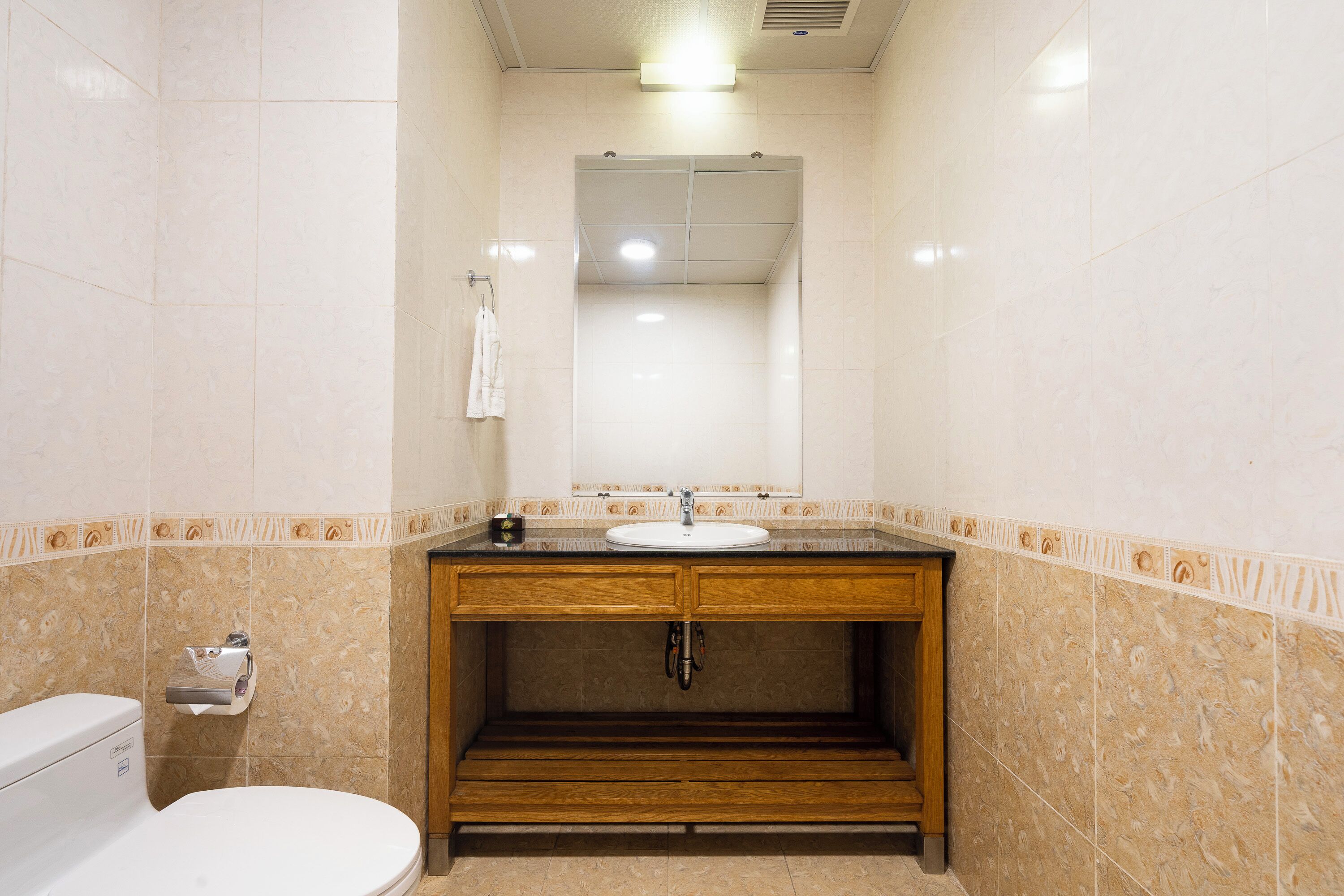 A bathroom with a toilet, sink, mirror, and wooden vanity.