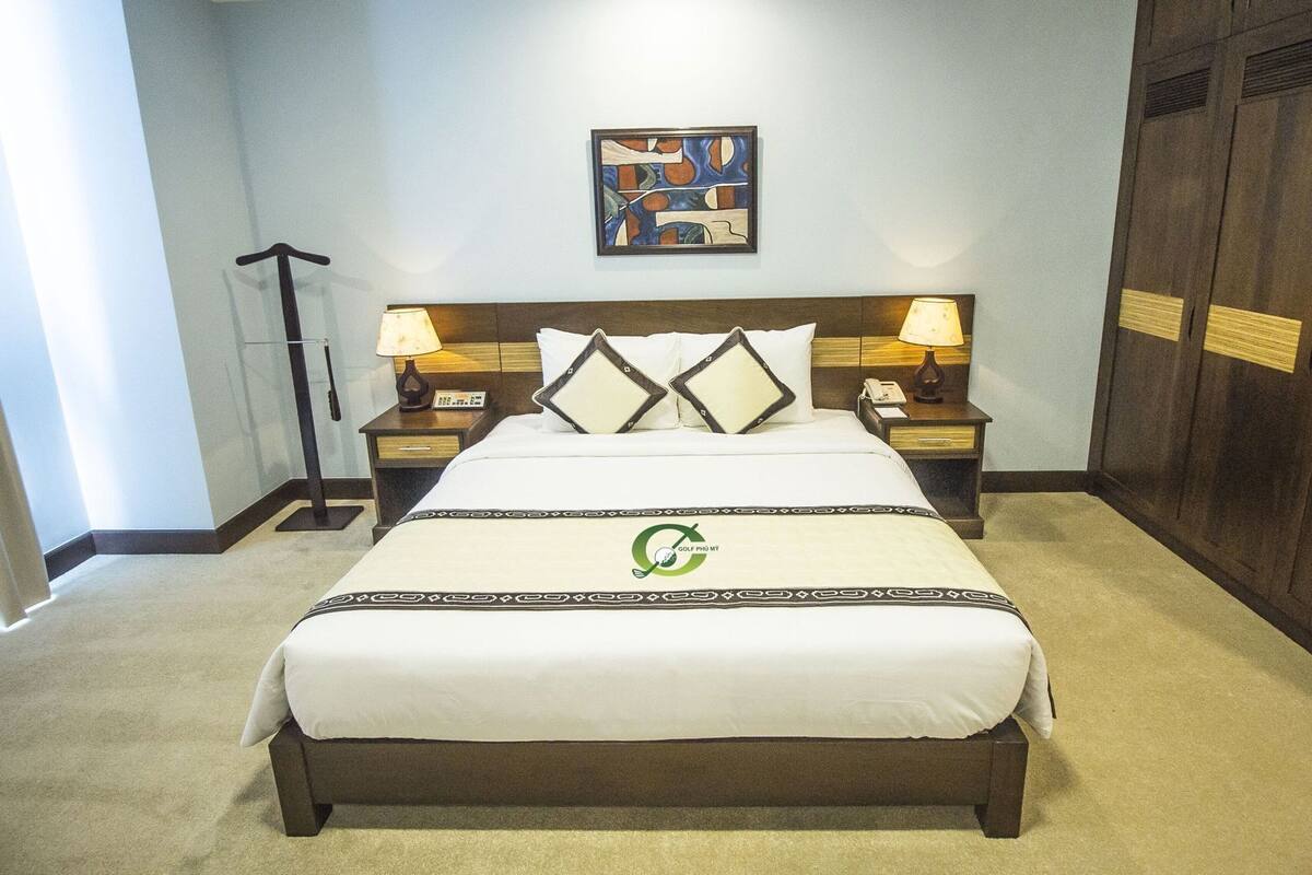 A hotel room with a bed, two bedside tables with lamps, a wall-mounted artwork, and a wardrobe.