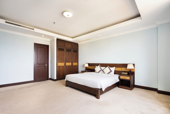 Una habitación de hotel con una cama grande, armario de madera, mesita de noche con lámpara y un respiradero en el techo.