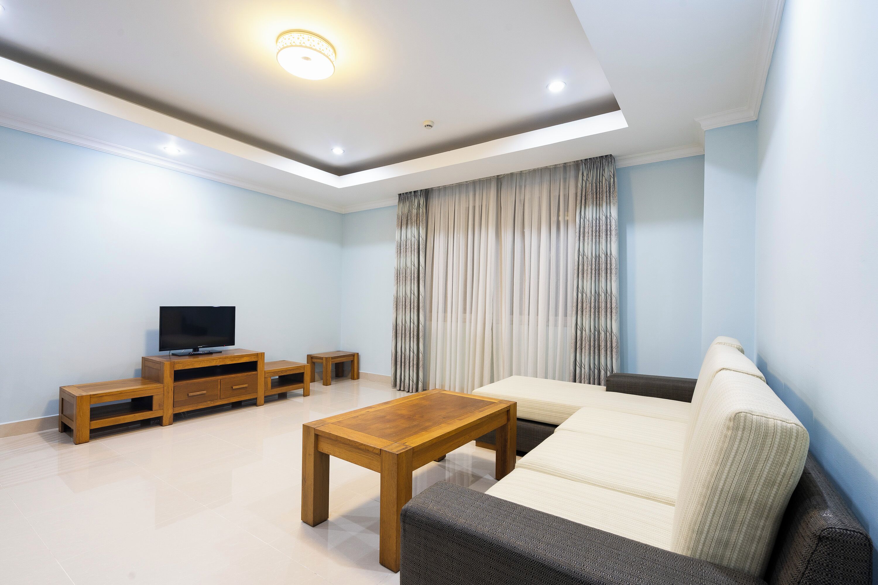 A living room with a sofa, a coffee table, a TV stand, and curtains.