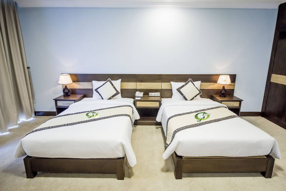 A hotel room with two beds, a wooden headboard, bedside tables with lamps, and a telephone.