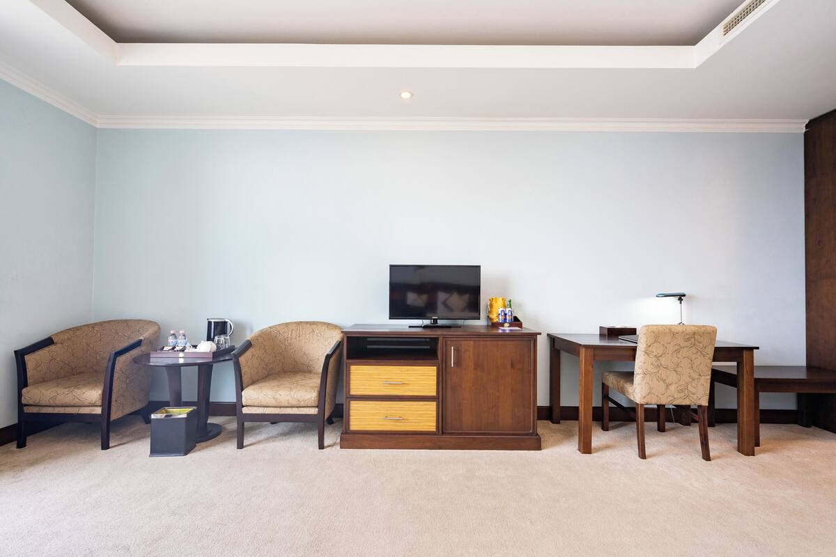 A hotel room with a TV, two armchairs, a wooden desk, and a cabinet.